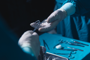 A surgeon hands over surgical scissors to a colleague during a medical procedure, with various surgical tools laid out on a sterile table in the background.